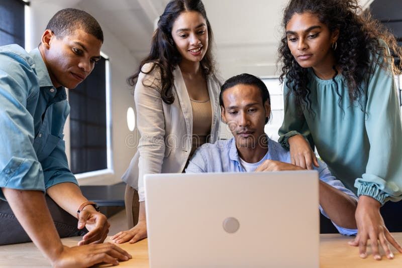 Four diverse colleagues collaborating on a laptop in a modern office.