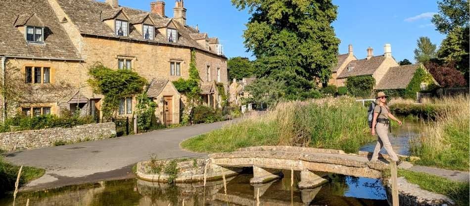 Walker crossing a stone footbridge in a picturesque English village