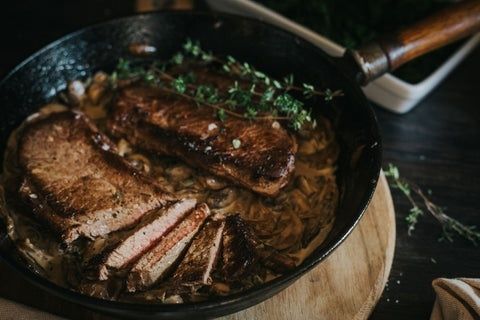 Seared game steak with sauce, onions, herbs, and sliced meat in a skillet